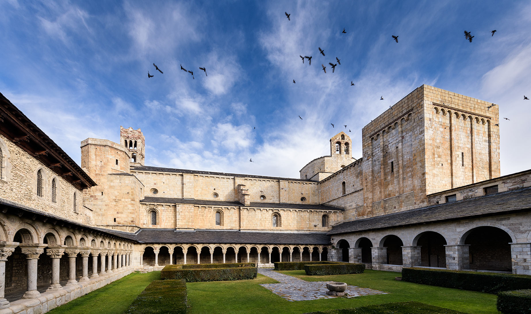 Vista del Claustro con la Catedral en el fondo y pájaros en el cielo. 