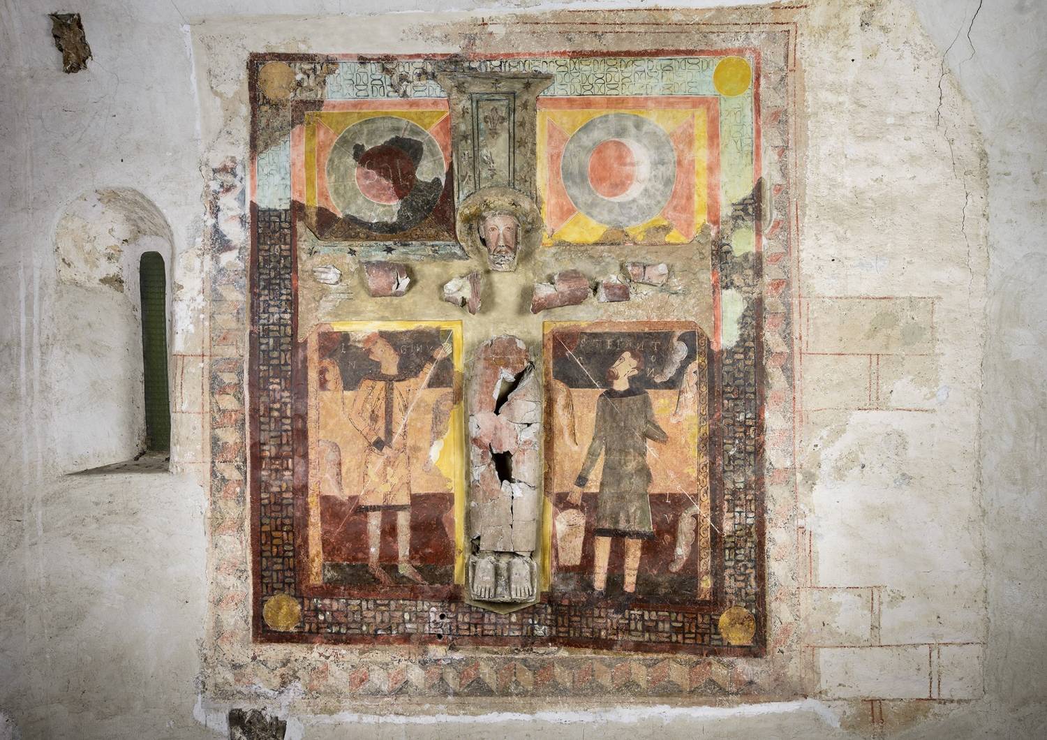 Majestat romànica d'estuc del segle XII envoltada d’una escena pictòrica mural que representa la crucifixió amb Longinos i Stefanon acompanyats del Sol i la Lluna. 