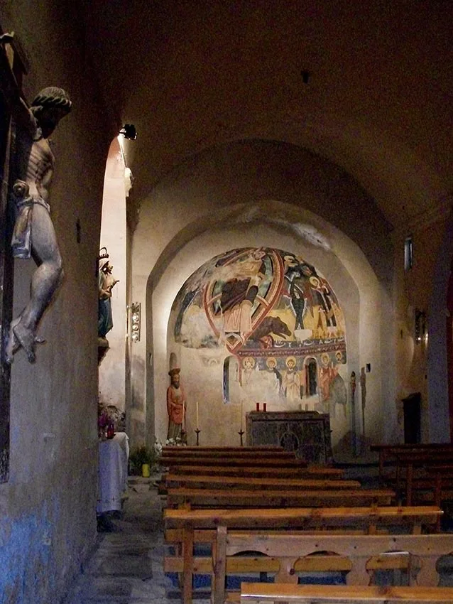 Vista de l'interior de l'església de Sant Pau i Sant Pere d'Esterri de Cardós amb les pintures murals de l'absis i una imatge de Crist a la paret lateral. 