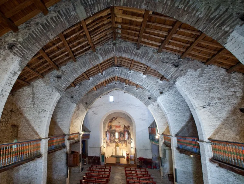 Vista de l'església de Santa Maria d'Àneu des del cor amb bancs i les pintures murals a l'absis. 